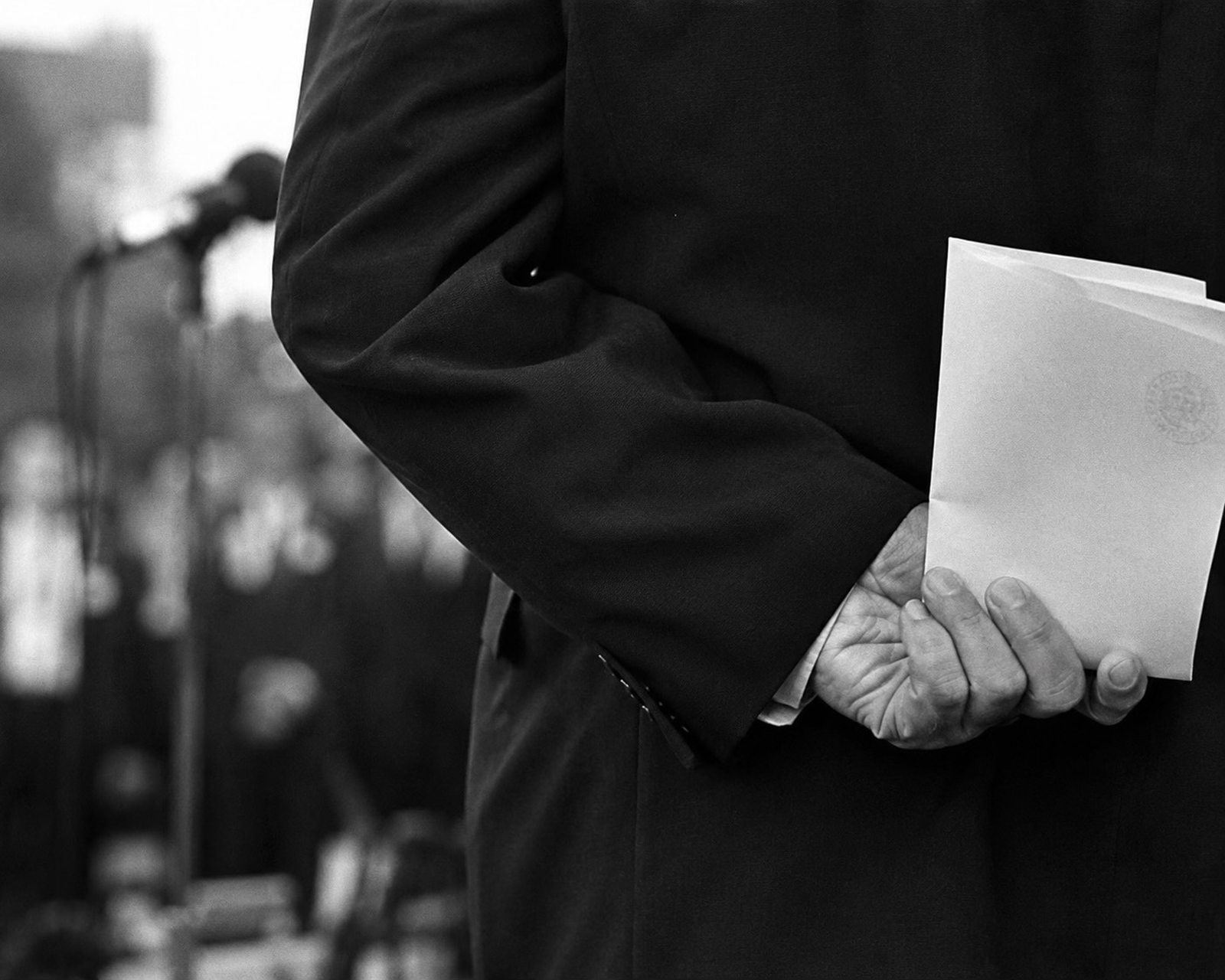 Orador sosteniendo un discurso a la espalda ante un micrófono, en blanco y negro